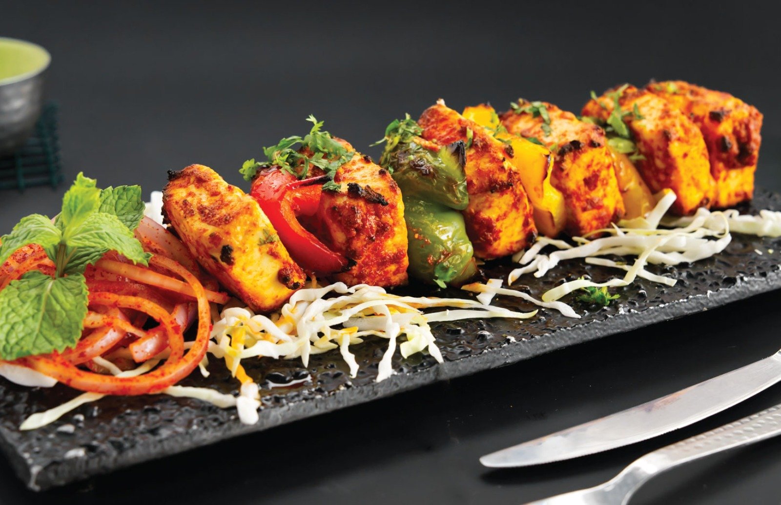 Dhinchak serving the best Indian food in Croydon paneer kebab on a long black plate garnished with mint