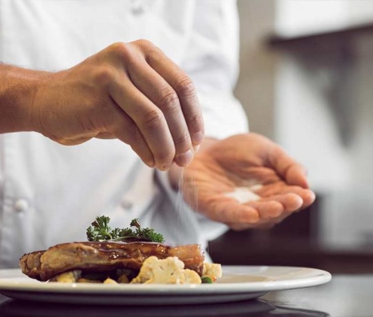Fine Indian Cuisine from Dhinchak, Croydon chef plating a meal, garnishing with salt