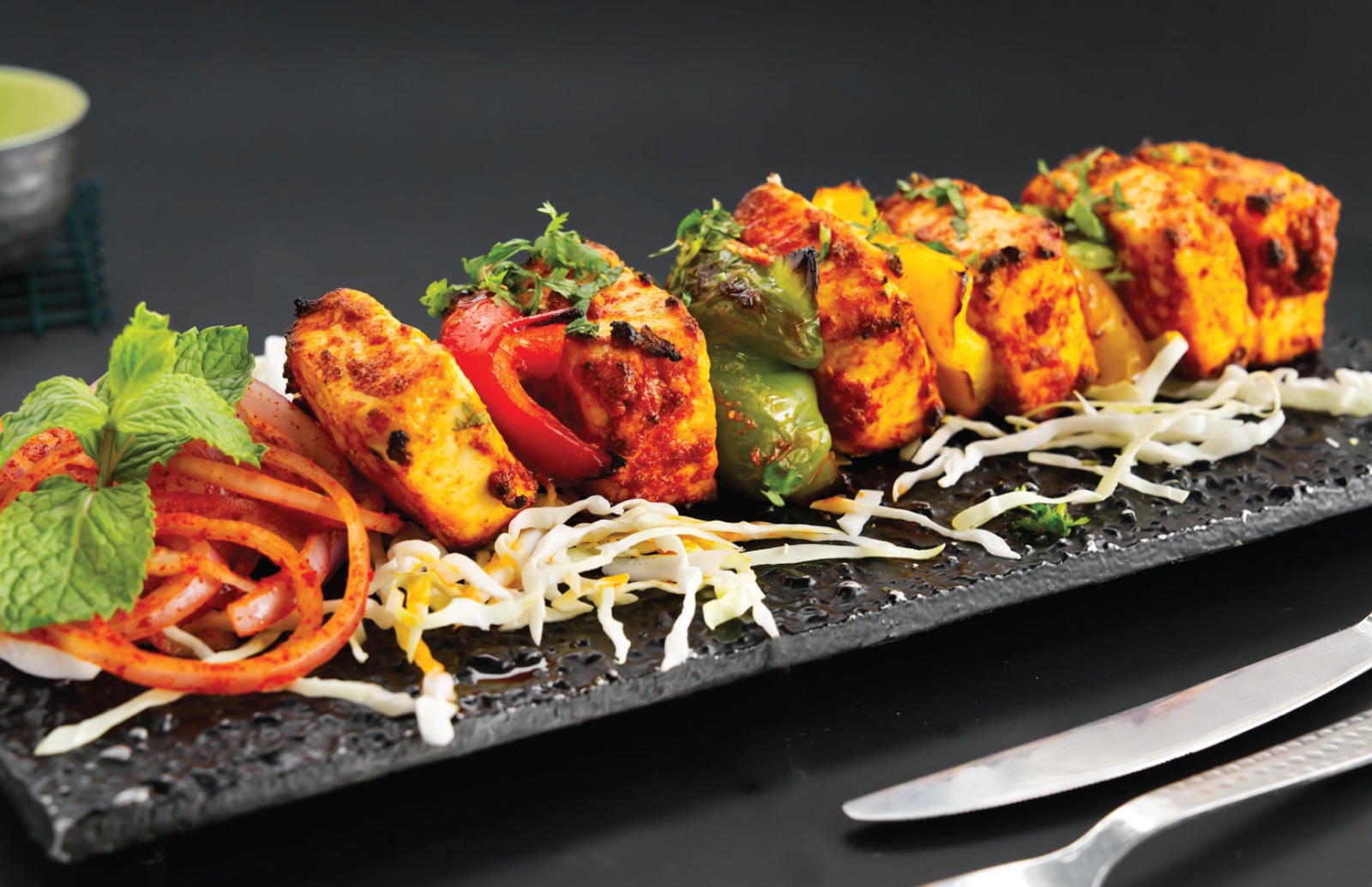 paneer kebab on a long black plate garnished with mint