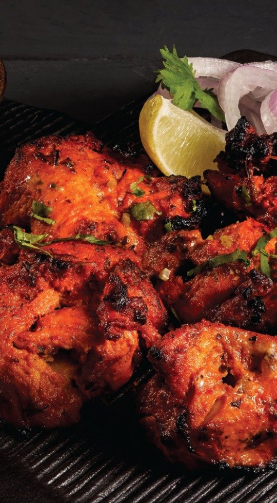 chicken tikka on a black plate served with lemon and onions